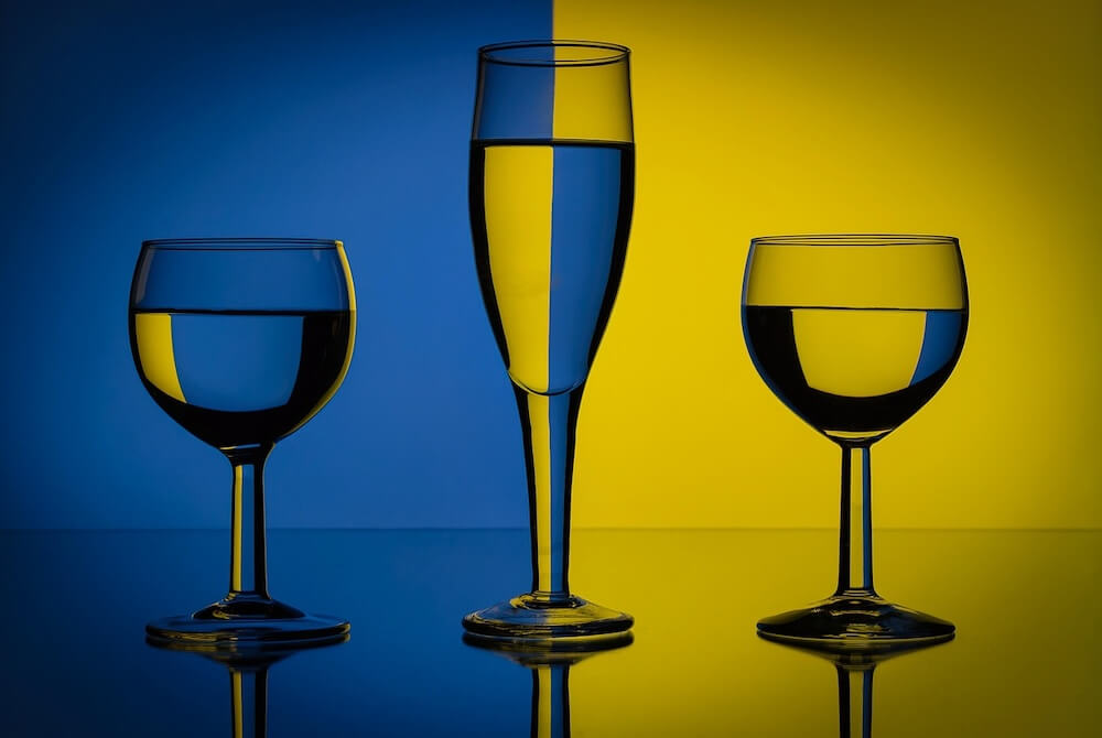 Gelbe Strahlen, die von rechts kommen und ins linke Glas treffen, werden zu uns hin gebrochen, so dass wir sie vor blauem Hintergrund sehen.